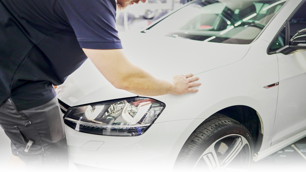 Das Bild zeigt ein weißes Auto in der MM KFZ Werkstatt. Ein KFZ Mechaniker untersucht die Spaltmaße.