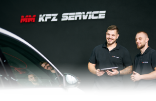 Zwei MM-KFZ Service Mitarbeiter stehen lächelnd in der Werkstatt und begutachten ein Auto.