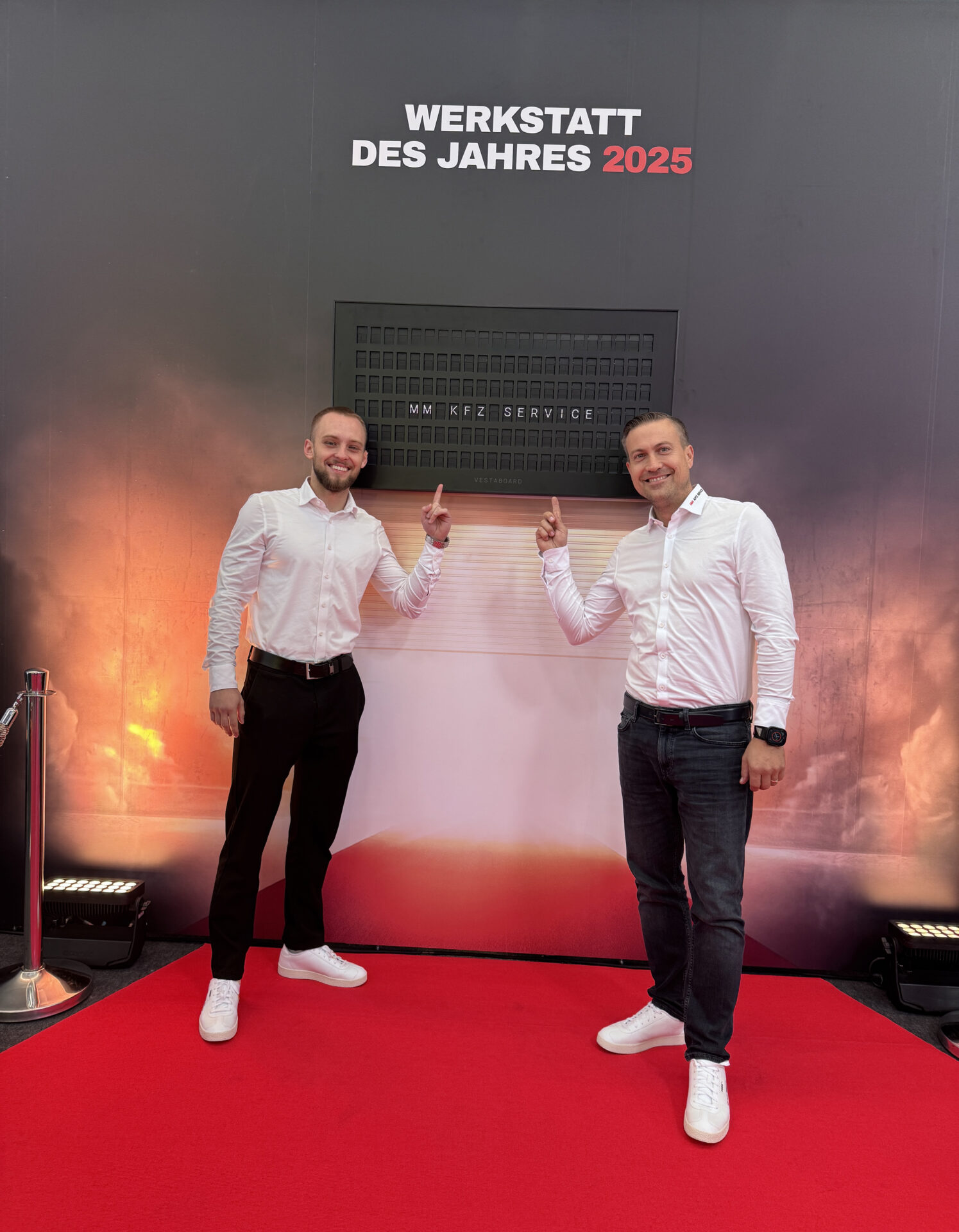 Zwei Männer auf dem roten Teppich, die auf den Namen der Werkstatt "MM KFZ Service" zeigen. Der Name der Werkstatt steht unter der Headline "Werkstatt des Jahres 2025"